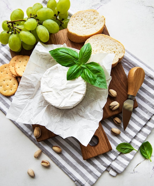 Vista de cerca de queso camembert, uva, nueces y miel en la tabla de cortar sobre la mesa blanca