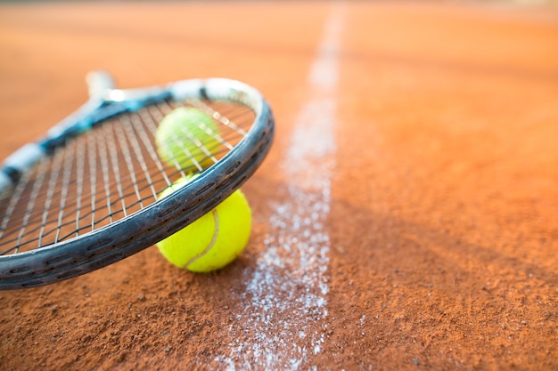 Vista de cerca de la raqueta de tenis y las bolas en la cancha de tenis de arcilla