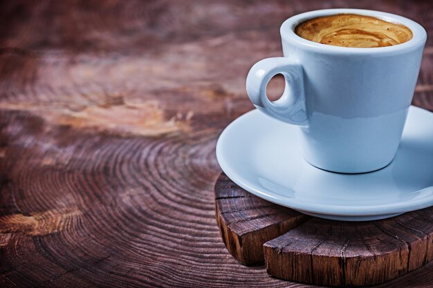 Vista de cerca de la taza de café con leche con capuchino en el tronco de un árbol cortado en cruz de madera vintage