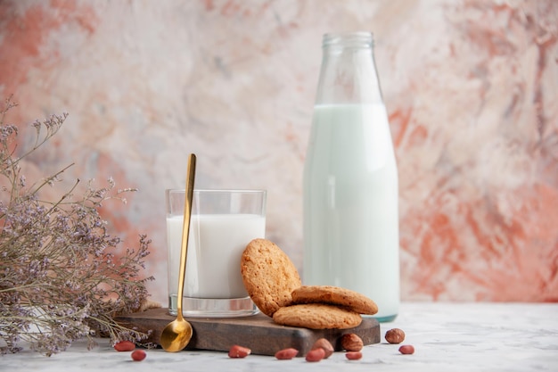 Vista de cerca de la taza de vidrio y la botella llena de galletas de leche en la flor de la tabla de madera sobre fondo de colores mezclados