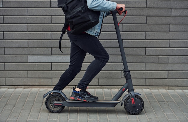 Vista de cerca de un tipo con ropa informal que monta una moto eléctrica al aire libre durante el día soleado