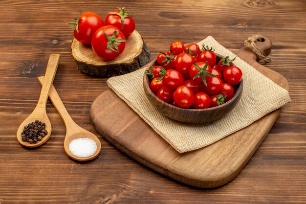 Vista de cerca de tomates frescos en un tazón marrón en una tabla de cortar en una tabla de madera especias con espacio libre