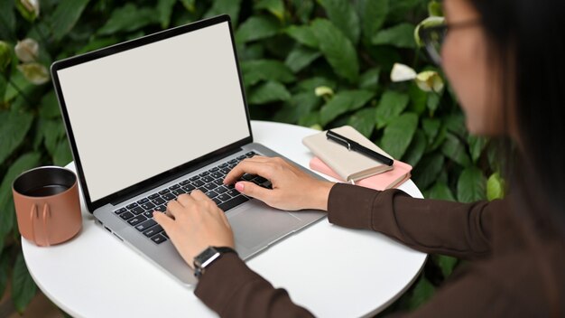 Vista de cerca de la trabajadora de oficina escribiendo en el teclado de la computadora portátil en la mesa redonda en el jardín en casa