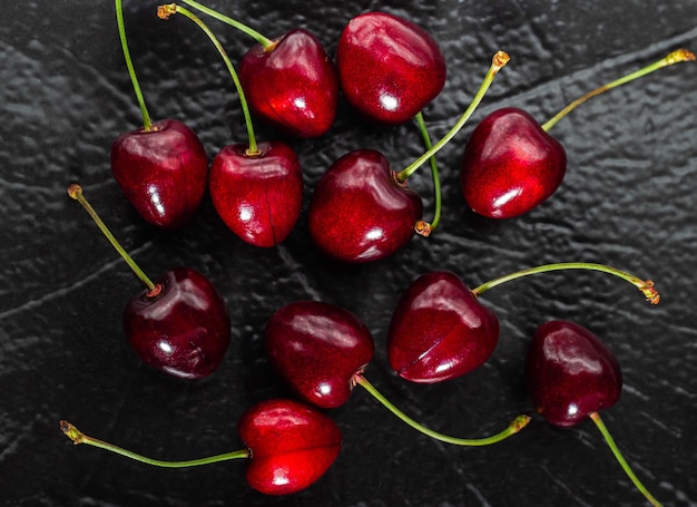 Vista cercana de bayas de cereza jugosas rojas en placa con textura oscura