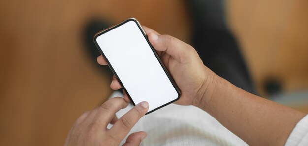 Vista cercana del empresario tocar el teléfono inteligente de pantalla en blanco mientras está de pie en la sala de oficina