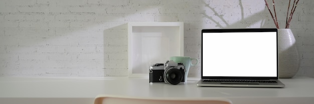 Vista cercana del espacio de trabajo mínimo con pantalla en blanco portátil, cámara, decoraciones y copia espacio en la mesa blanca