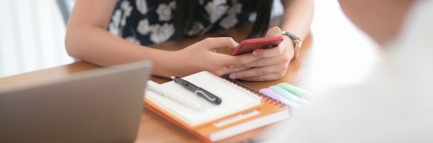 Vista cercana de una estudiante universitaria usando un teléfono inteligente para relajarse después de hacer su tarea