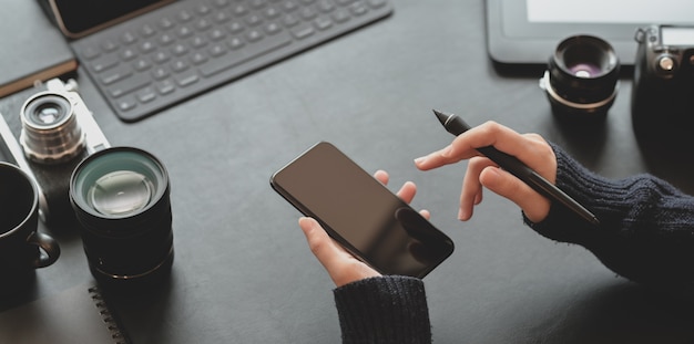 Vista cercana de la fotógrafa con smartphone en lugar de trabajo elegante y oscuro