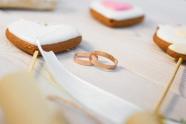 Vista cercana de galletas en forma de corazón bisquits en bastón y anillos de boda.