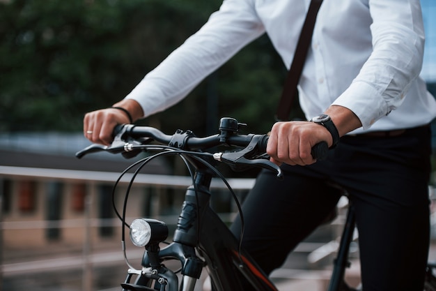 Vista cercana. Hombre de negocios en ropa formal con bicicleta negra está en la ciudad.