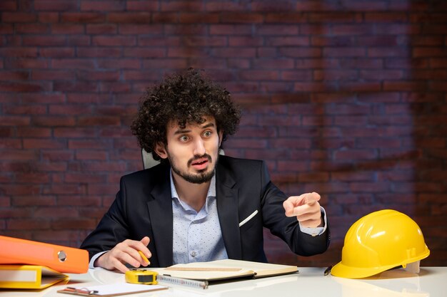 Vista cercana ingeniero masculino sentado detrás del lugar de trabajo en traje de trabajo de constructor de agenda de trabajo de negocios contratista