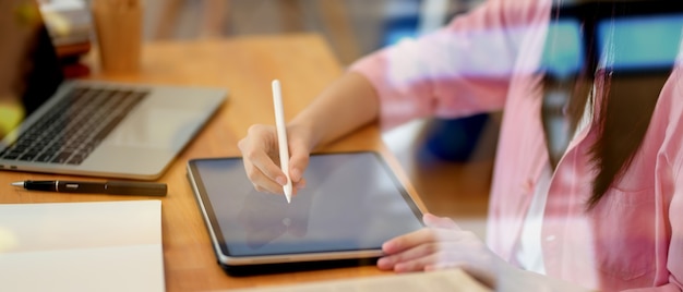 Vista cercana de la joven estudiante que trabaja en su proyecto con tableta, vista a través de la vista de vidrio