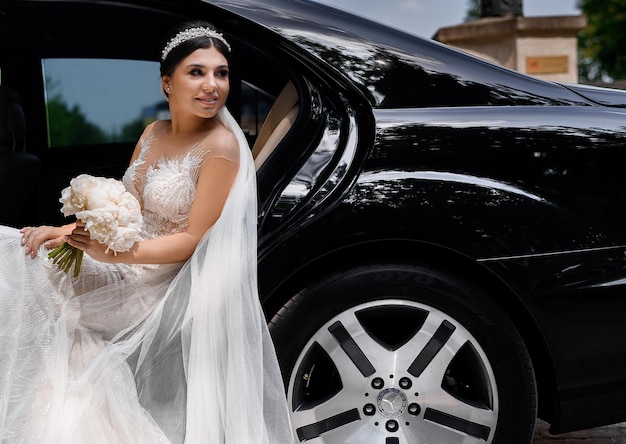 Vista cercana de la linda novia con aro de joyería y velo largo en la cabeza vestida con un vestido de encaje de novia sonriendo y mirando hacia otro lado mientras se sienta dentro del interior del automóvil Concepto de espacio de copia y boda