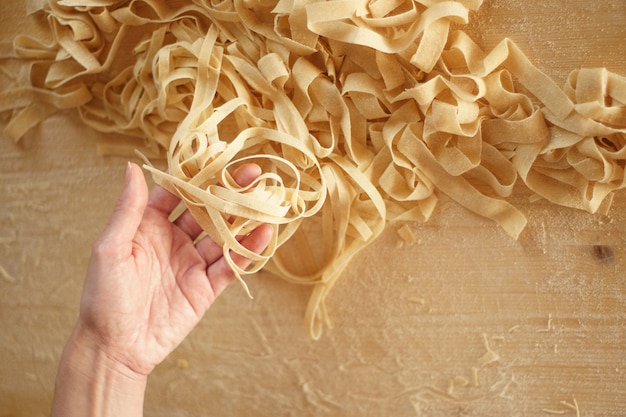 Vista cercana de la mano de la mujer levantando fettuccine fresco en la mesa de trabajo de madera a la luz solar natural