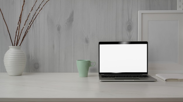 Vista cercana del moderno espacio de trabajo con una computadora portátil de pantalla en blanco en el escritorio de mármol con pared rústica moderna blanca