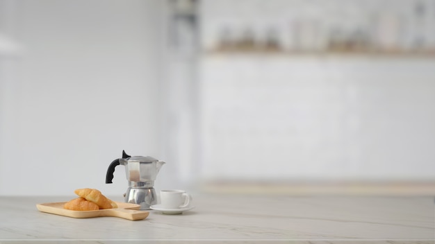 Foto vista cercana de moka pot, taza de café, croissant y copia espacio en mesa de mármol con sala de cocina borrosa