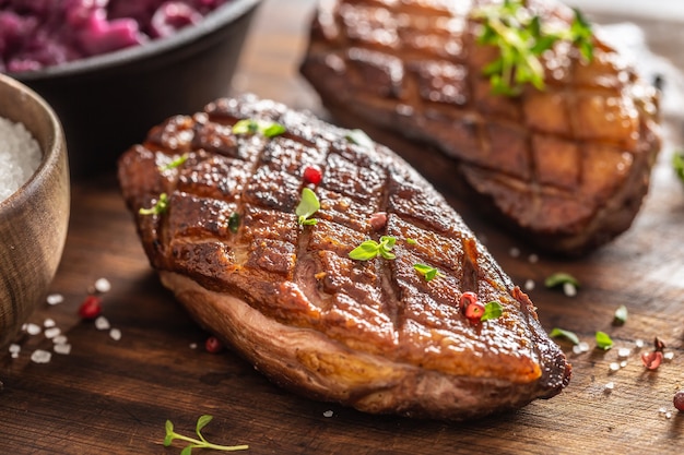 Vista cercana de pechugas de pato recién asadas con condimento de pimienta y hierbas frescas en la parte superior.