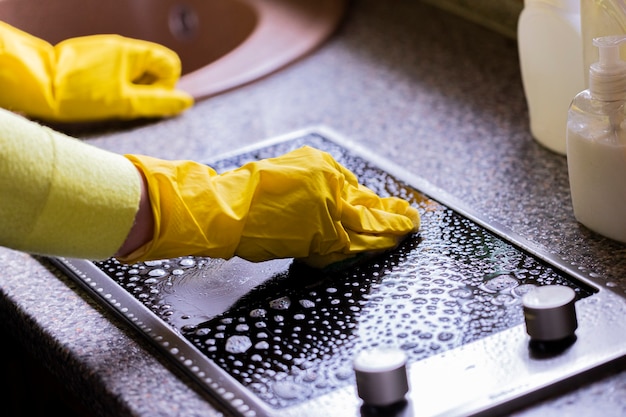 Foto vista cercana de la persona en guantes de goma amarillos cocina de limpieza, elimina la grasa dura