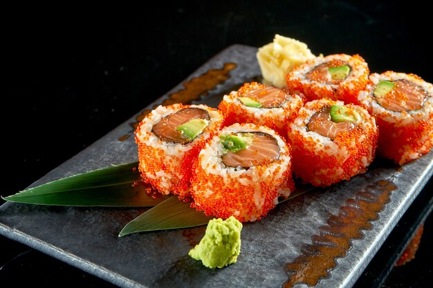 Vista cercana de sabroso uramaki con salmón, aguacate y caviar tobiko. Cocina tradicional japonesa. Entrega de comida. Aislado en negro