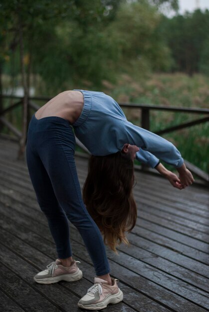 Foto la vista de una chica con cuerpo atlético en traje de gimnasia está haciendo ejercicios en el parque en un clima nublado y lluviosoxa