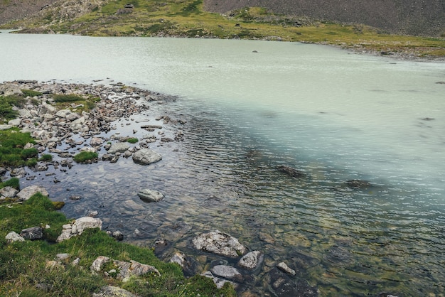 Vista desde la cima al lago de montaña turquesa con agua transparente. Paisaje de montaña atmosférica con superficie de agua turquesa del lago glaciar entre piedras y hierba. Vista desde arriba al lago de las tierras altas.