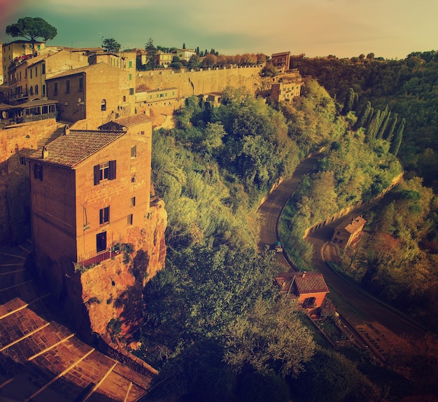 Vista a la ciudad medieval de toba Pitigliano con árboles verdes y escaleras de adoquines, viajes de fondo vintage de Italia al atardecer