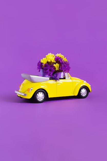 Vista de un colorido auto convertible amarillo con un ramo de flores en un rosa que deja la nube azul en forma de corazón. Concepto de vacaciones, entrega, arte, transporte