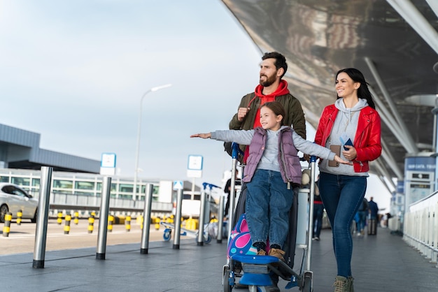 Vista completa de la familia y los niños con equipaje en la terminal del aeropuerto vuelan juntos de vacaciones. Niña feliz jugando en el avión