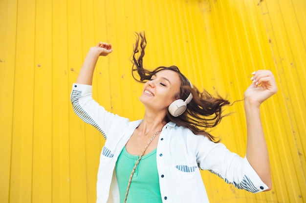 Foto una vista completa de una hermosa niña alegre saltando mientras escucha una melodía aislada contra un fondo amarillo brillante una mujer joven con auriculares bailando en la calle generación z