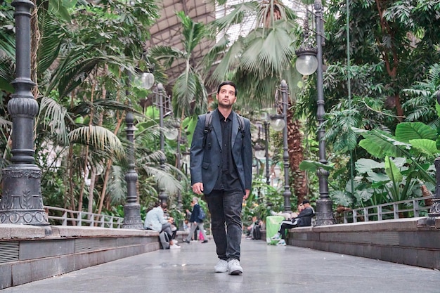 vista completa de un joven con ropa formal caminando por la ciudad rodeado de plantas