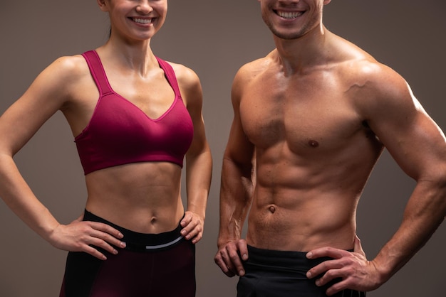 Vista cortada do homem atlético e mulher posando para a câmera antes do exercício de fitness no estúdio com parede marrom