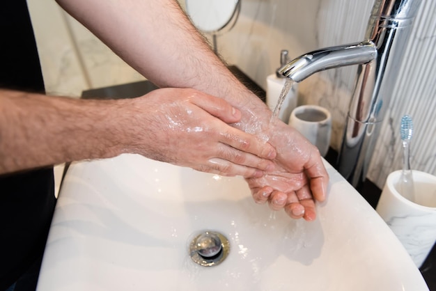Vista cortada do homem lavando as mãos no banheiro