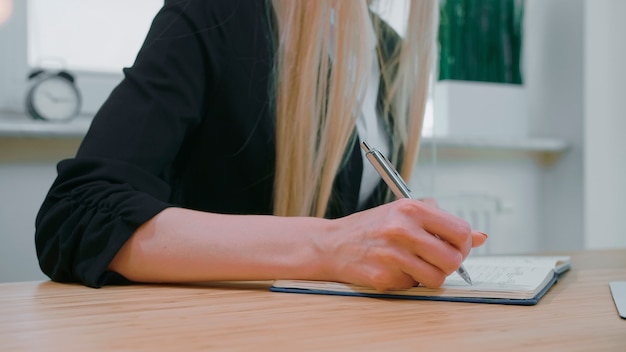 Vista de la cosecha de la mujer con el pelo largo y rubio en camisa casual brillante sentado en el escritorio de madera y escribiendo ...