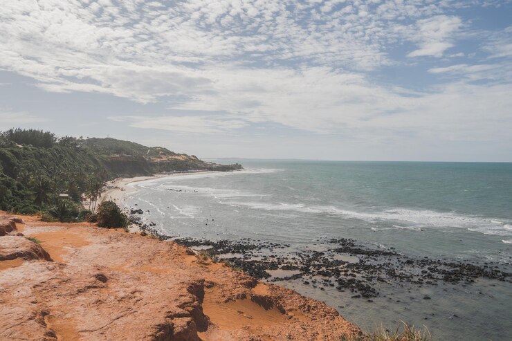 vista de la costa de una playa con rocas negras en la orilla en un día soleado con nubes cubriendo el cielo
