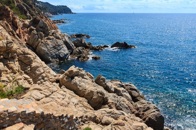 Vista de la costa rocosa del mar de verano con destellos soleados en la superficie del agua y escaleras pedregosas (Costa Brava, España).