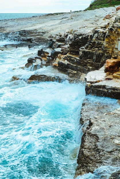 Vista da água com ondas com penhasco rochoso