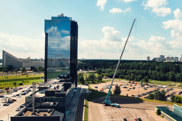 Vista da altura do guindaste mais alto do carro, que está aberto no estacionamento próximo ao prédio de vidro da cidade e pronto para funcionar. o guindaste móvel mais alto é implantado no local.