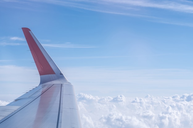 Vista da asa de um avião voando no céu azul com nuvens brancas embaixo