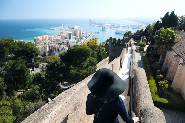 Vista da cidade de málaga com uma mulher de chapéu na escada de alcazaba