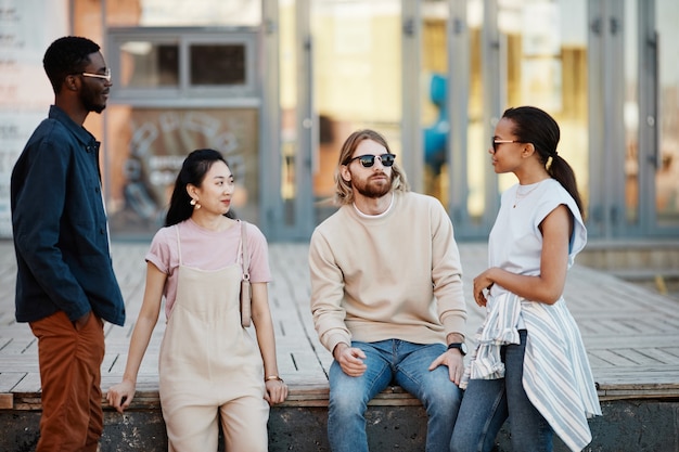 Vista da cintura para cima em um grupo diversificado de jovens contemporâneos conversando ao ar livre em um ambiente urbano de cidade