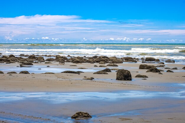 Vista da costa do mar sob o céu azul repleto de pedras em um terreno arenoso