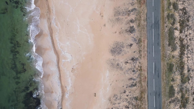 Vista da estrada ao longo da costa arenosa do mar do drone voando acima da estrada vazia e da praia