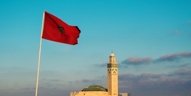 Foto vista da famosa mesquita hassan ii e uma bandeira marroquina agitada contra o céu - casablanca, marrocos