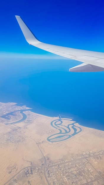 Vista da janela do avião no céu azul e terra com paisagem de mar deserto e canais nos Emirados