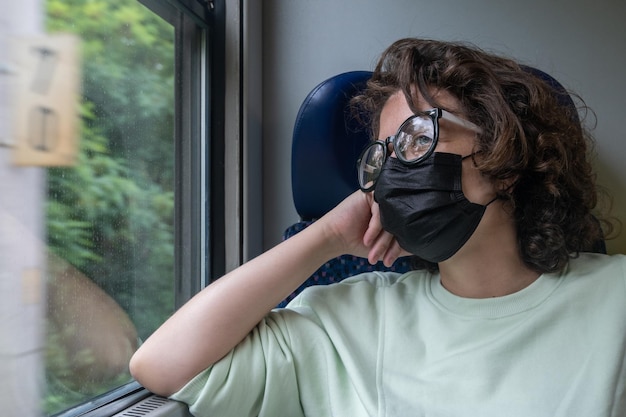 Vista da jovem viajando de trem durante a pandemia usando óculos e máscara preta