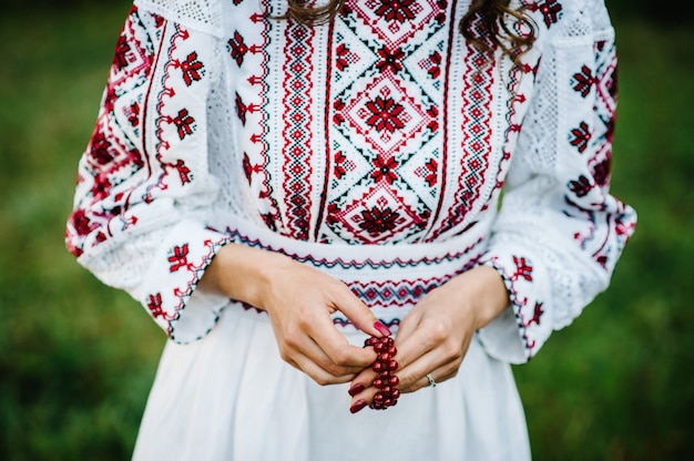 Vista da mão feminina com laca vermelha nas unhas e usa uma pulseira de pedras preciosas em estilo rústico.