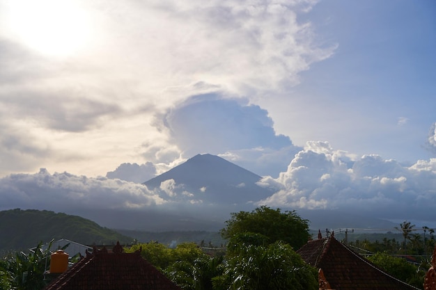Foto vista da montanha contra um fundo de palmeiras e um campo de milho panorama do vulcão agung coberto de nuvens antes do pôr-do-sol