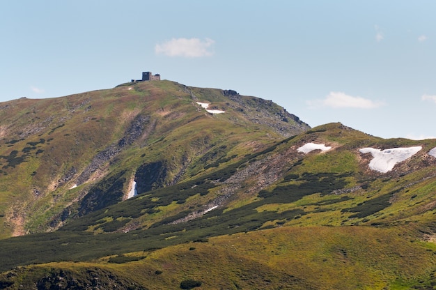 Vista da montanha no verão com neve na encosta (com ruínas do observatório em Chornogora Ridge, Ucrânia)