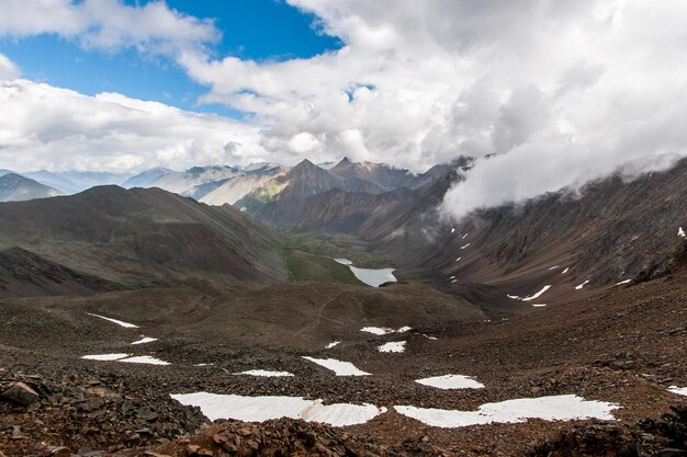 Vista da passagem da montanha para o vale Abaixo do lago e da neve Ao longe há montanhas e nuvens acima deles Horizontal