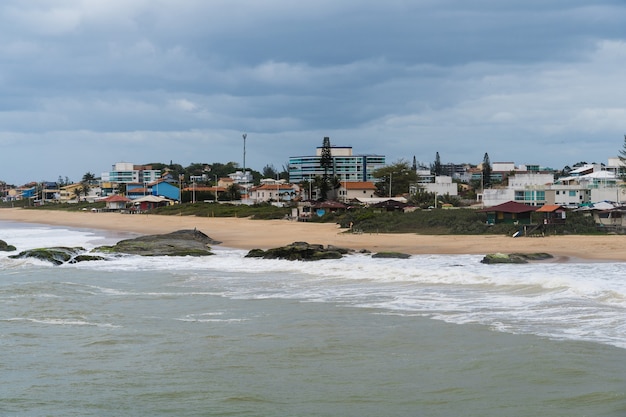 Foto vista da praia de rio das ostras no rio de janeiro com céu nublado e algumas nuvens pesadas. mar forte e areia amarelada.